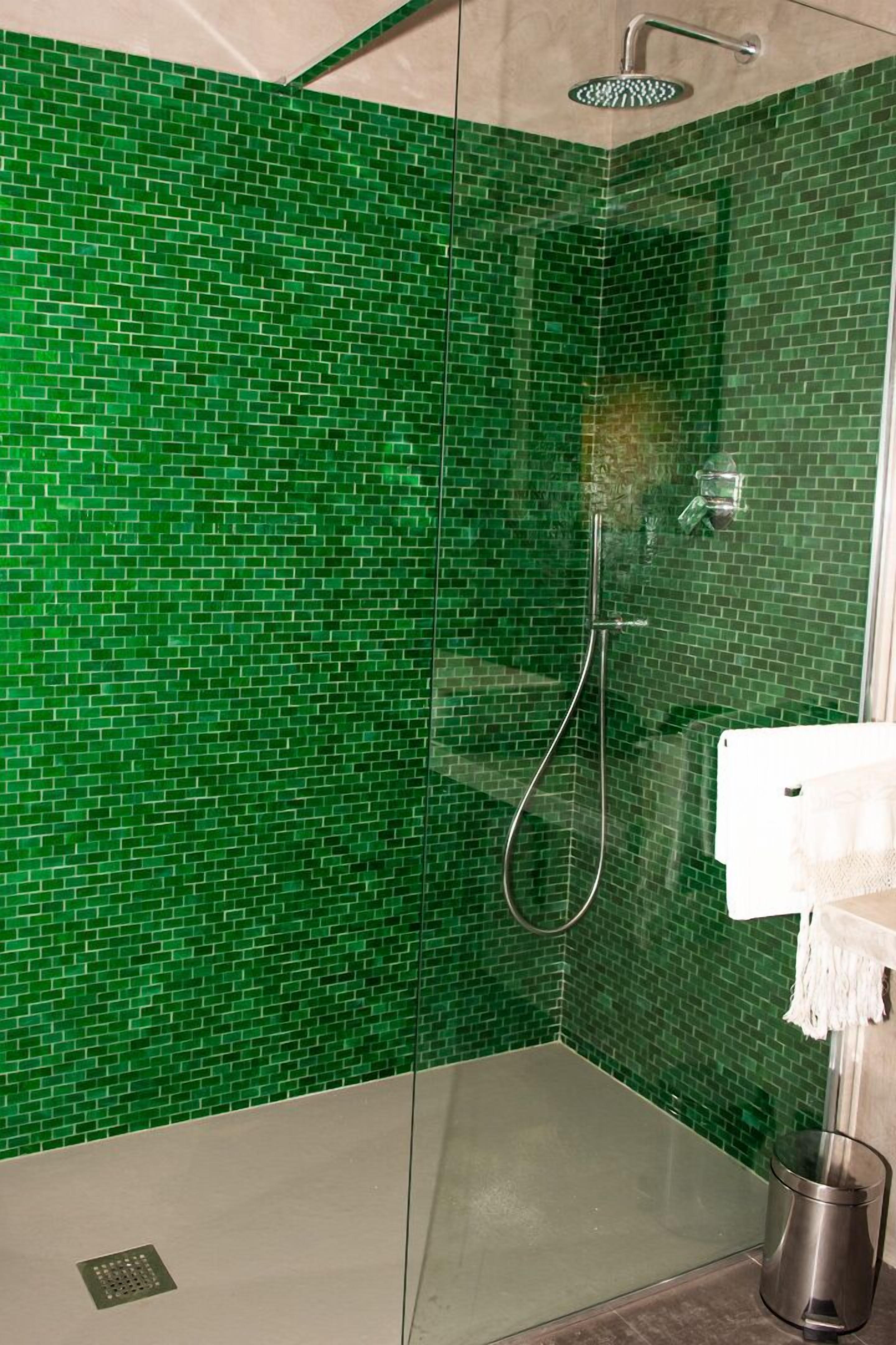 Ducha con cerramiento de vidrio y pared de mosaicos verdes.