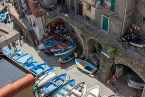 A narrow street with boats docked along the sides, a stone archway, and buildings with balconies.