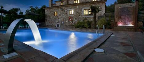 A stone building with a swimming pool, a fountain, and a night sky.