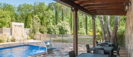 Un área de piscina al aire libre con suelo a cuadros, rodeada de mesas y sillas, bajo una pérgola de madera.