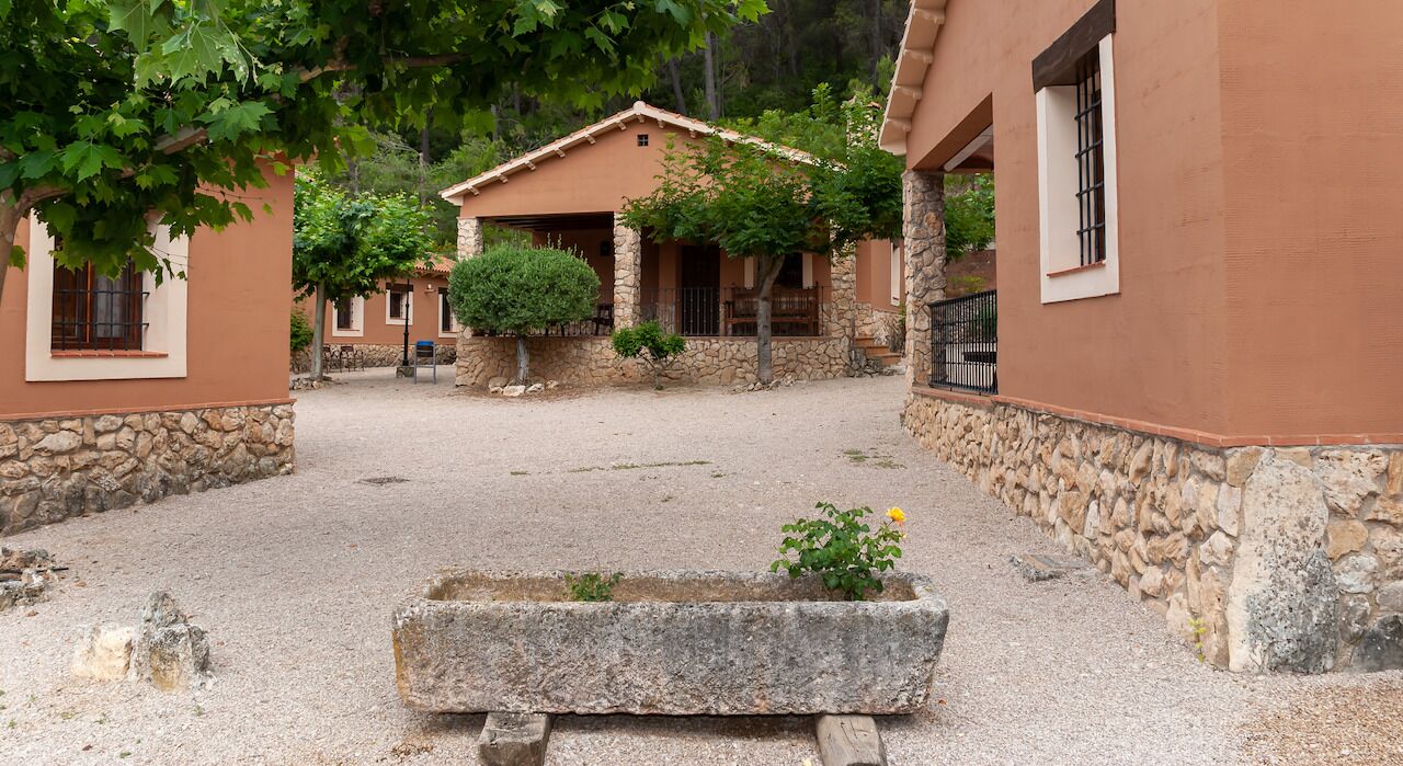 A courtyard with stone walls, a central planter with a plant, and a building with a tiled roof and windows.