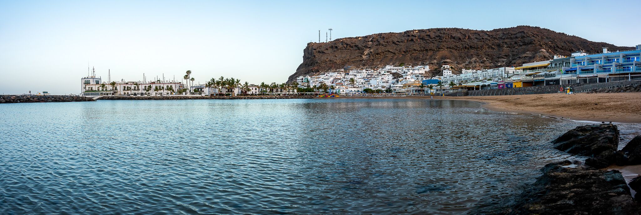 A coastal town with a prominent hill, white buildings, and a sandy beach.