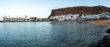A coastal town with a prominent hill, white buildings, and a sandy beach.