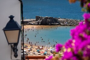 Une plage où l’on voit des gens nager et bronzer, une zone rocheuse et un lampadaire.