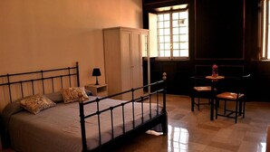A bedroom with a metal bed frame, a nightstand, a cabinet, a small table with a chair, and a window with natural light. - Rome: Luxury Apartment restructured in the heart of Rome (Roma)