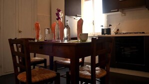 A dining area with a wooden table and chairs, a vase with flowers, and a kitchen in the background. - Rome: Luxury Apartment restructured in the heart of Rome (Roma)