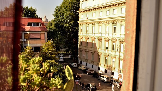 A street view with a building featuring classical architecture, parked cars, and pedestrians. - Rome: Luxury Apartment restructured in the heart of Rome (Roma)