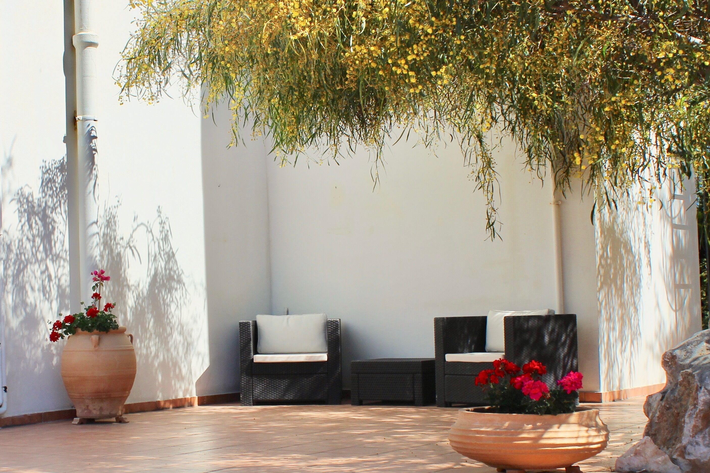 An outdoor seating area with two chairs and a table, surrounded by large planters with flowers.
