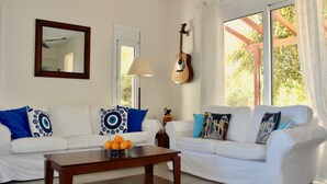 Ein Wohnzimmer mit zwei weißen Sofas, einem Holztisch mit Orangen, einer Gitarre und einer Lampe.
