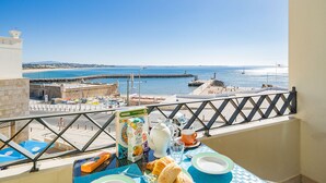 A balcony with a table set for breakfast, overlooking a coastal view with a clear sky. - Oceanside modern apartment [80] (Lagos)