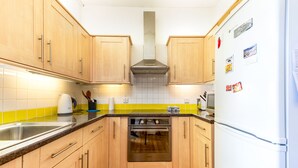 A compact kitchen with wooden cabinets, a stainless steel sink, a stove, and a white refrigerator. - Splendid, light and spacious apartment between Fulham and Kings Rd Chelsea. (London)