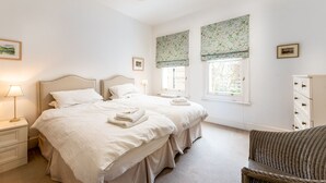 A bedroom with two beds, a nightstand with a lamp, a dresser, and a chair.