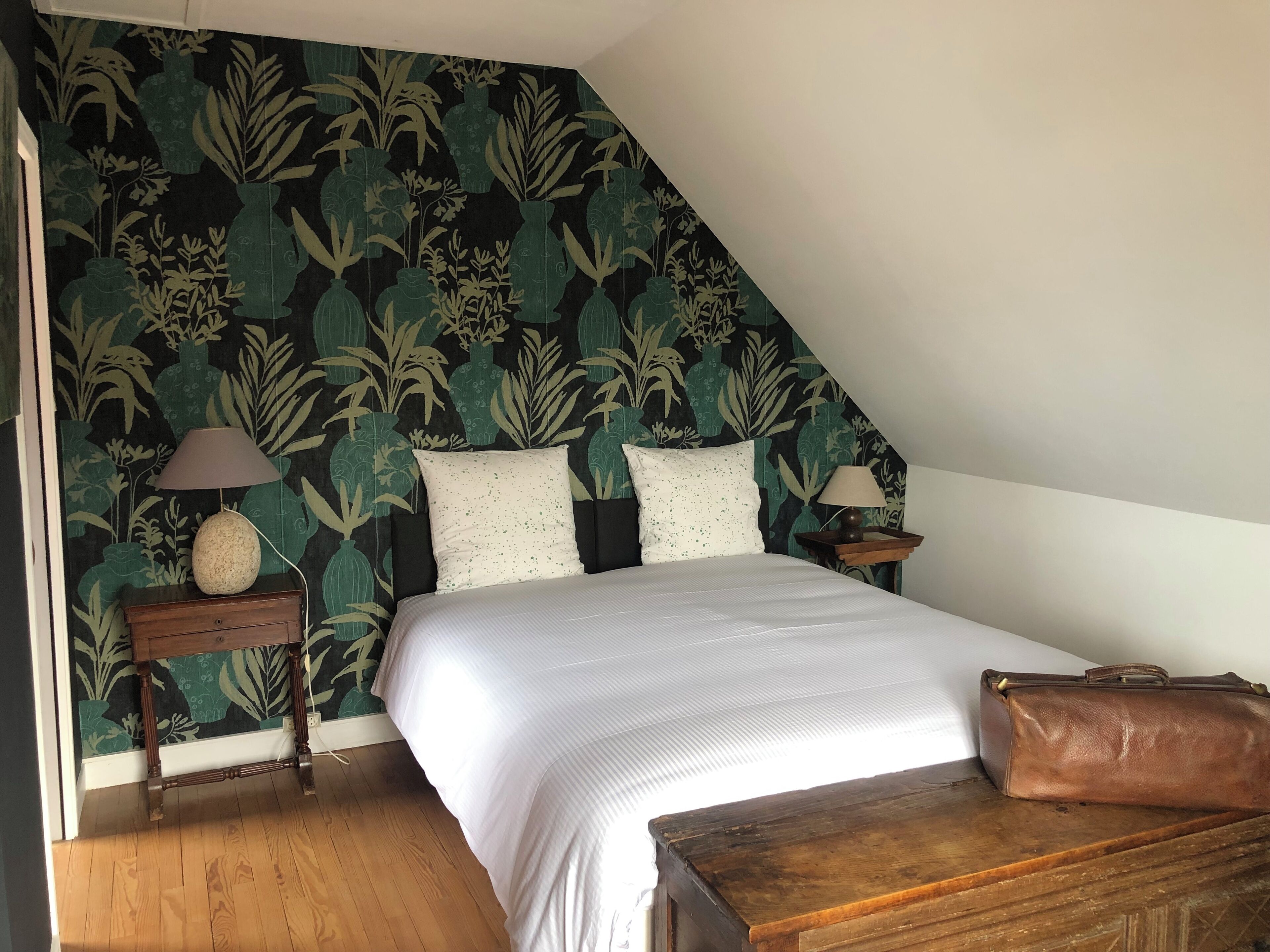 A bedroom with a bed, two bedside tables with lamps, a wooden bench, and a suitcase.