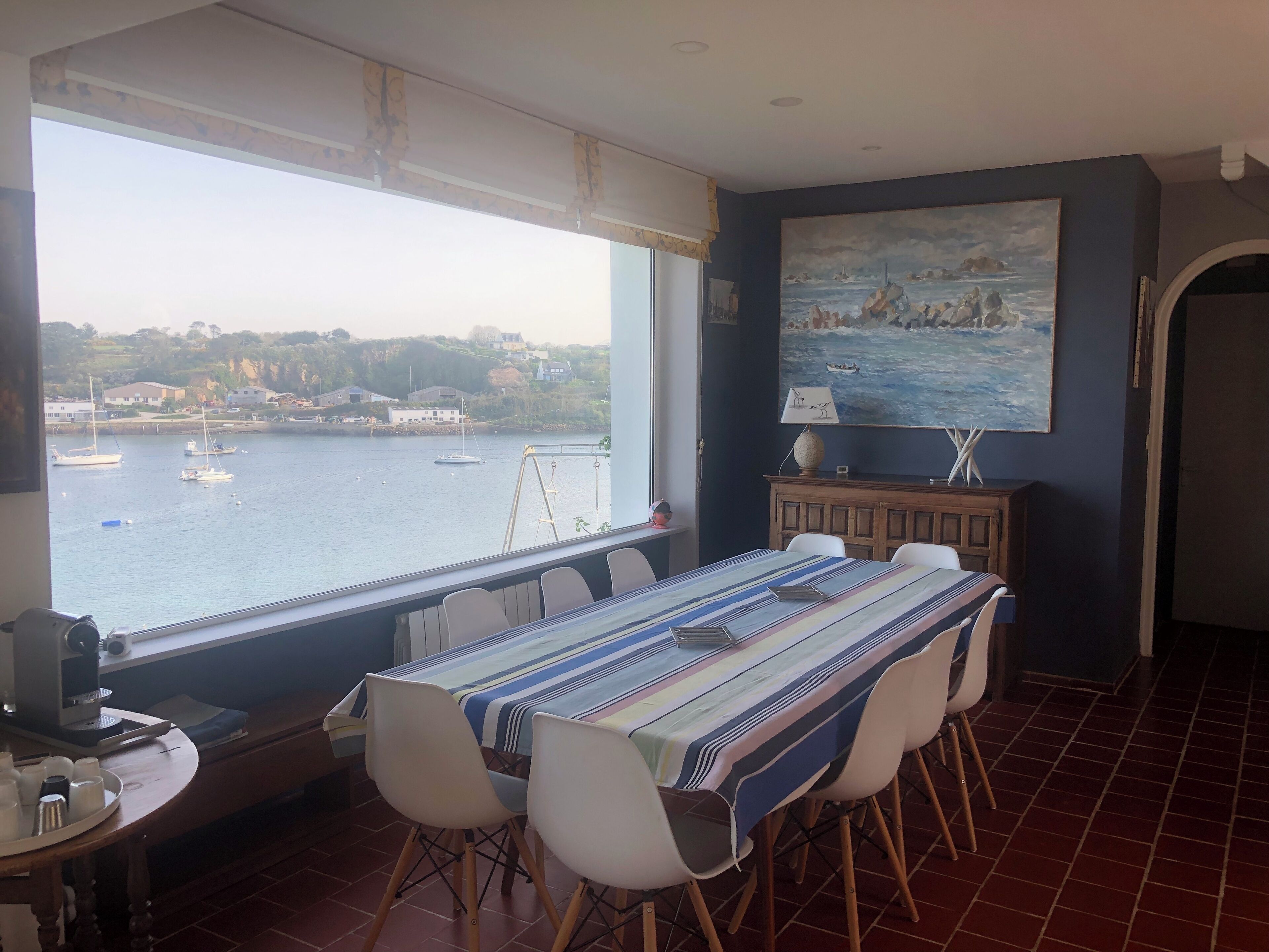 Un coin repas avec vue sur les bateaux qui naviguent, un tableau accroché au mur et une table dressée pour quatre personnes.