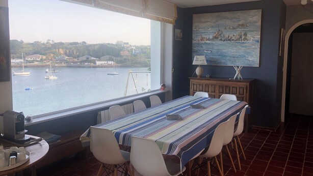 A dining area with a view of boats on the water, a painting on the wall, and a table set for four. - Saint Pabu: villa feet in water, 10 people (Saint-Pabu)