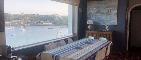 Un coin repas avec vue sur les bateaux qui naviguent, un tableau accroché au mur et une table dressée pour quatre personnes.