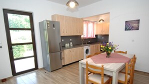A kitchen with wooden cabinets, a stainless steel refrigerator, a washing machine, and a dining table with chairs.