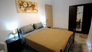 A bedroom with a bed, bedside tables, a nightstand, a painting, and a mirror.