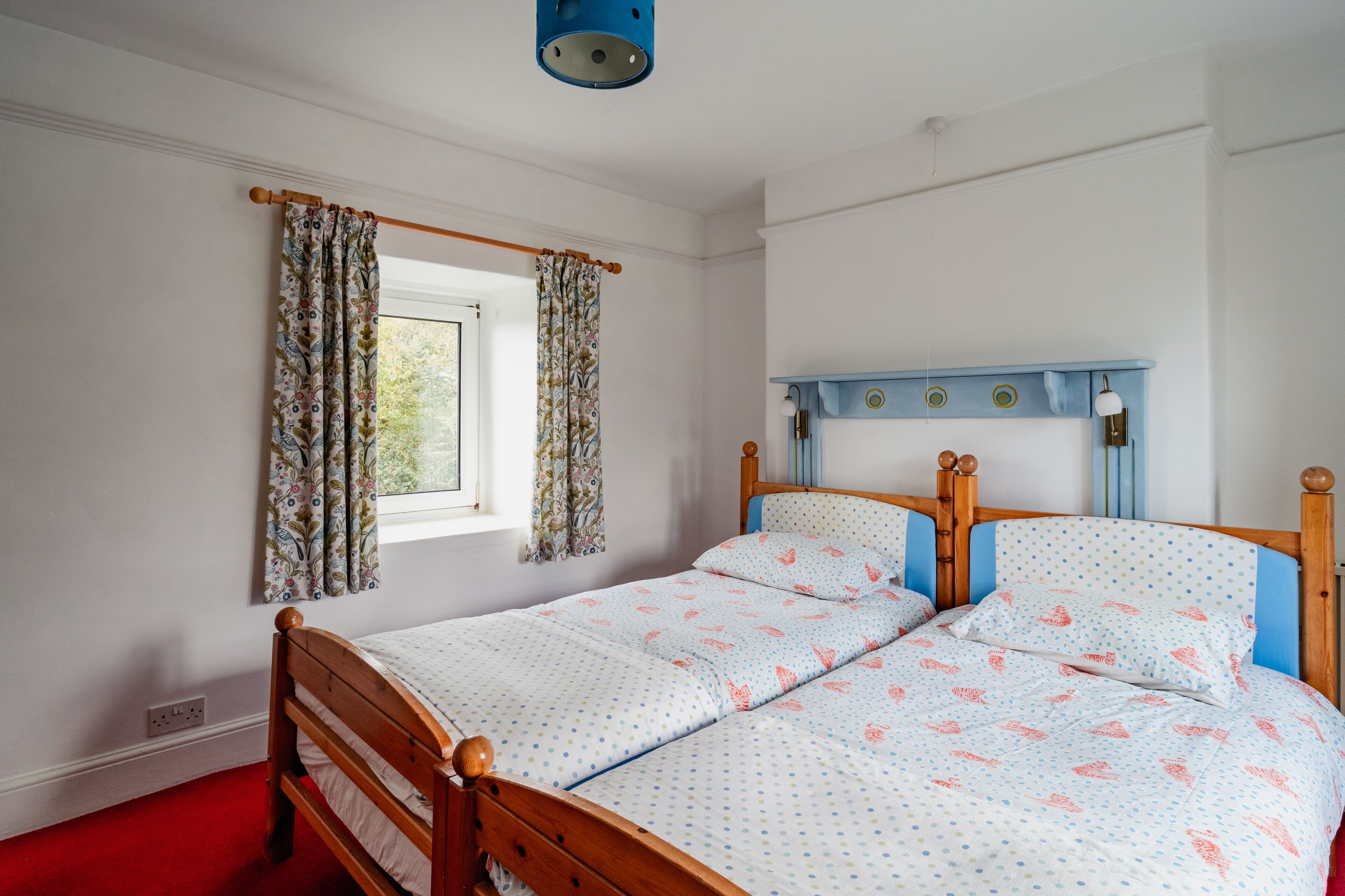 A bedroom with a wooden bed, floral curtains, a window, and a blue headboard.
