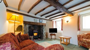 A cozy living room with a stone fireplace, wooden beams, a sofa, a television, and a window with curtains.