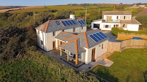 A modern house with solar panels on the roof, a large garden, and a view of the countryside.