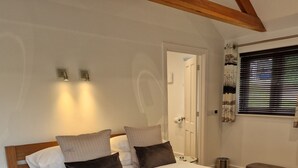 Un lit bien fait, avec une couette blanche et plusieurs oreillers, une table de chevet avec une lampe et une fenêtre équipée de stores.