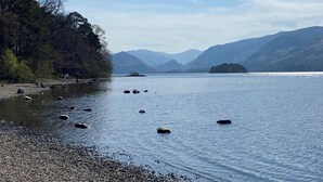 Un lac paisible, bordé d’une rive rocheuse, avec des montagnes qui se dessinent à l’horizon.