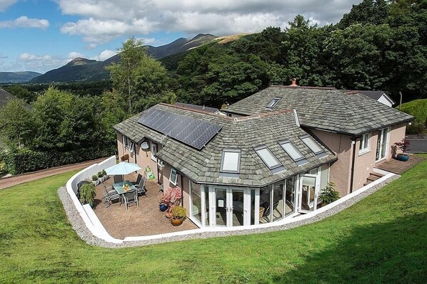 Una casa con un porche cubierto, paneles solares y vistas a las montañas.