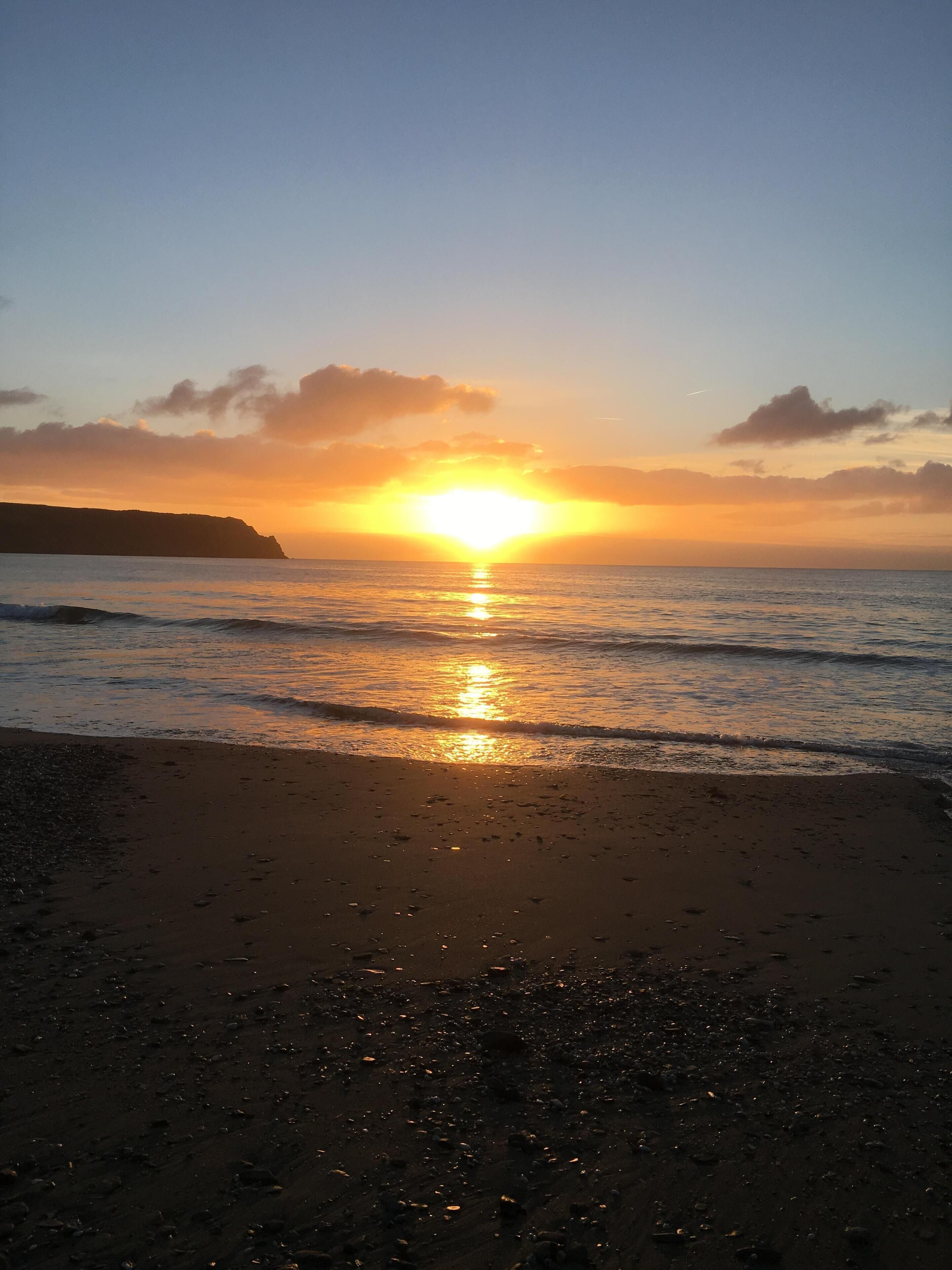 A beach at sunset with the sun reflecting on the water.