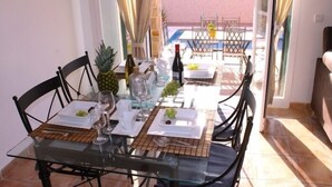 Une table à manger dressée avec de la verrerie, des assiettes et une bouteille, donnant sur une piscine et un espace de détente extérieur.