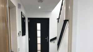 Ein Flur mit einer schwarzen Tür, einer Treppe und einem Lichtschalter an der Wand.