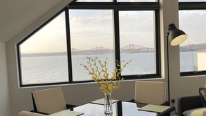 Ein Essbereich mit Blick auf eine Brücke über dem Wasser, eine Vase mit gelben Blumen und eine Tischlampe.