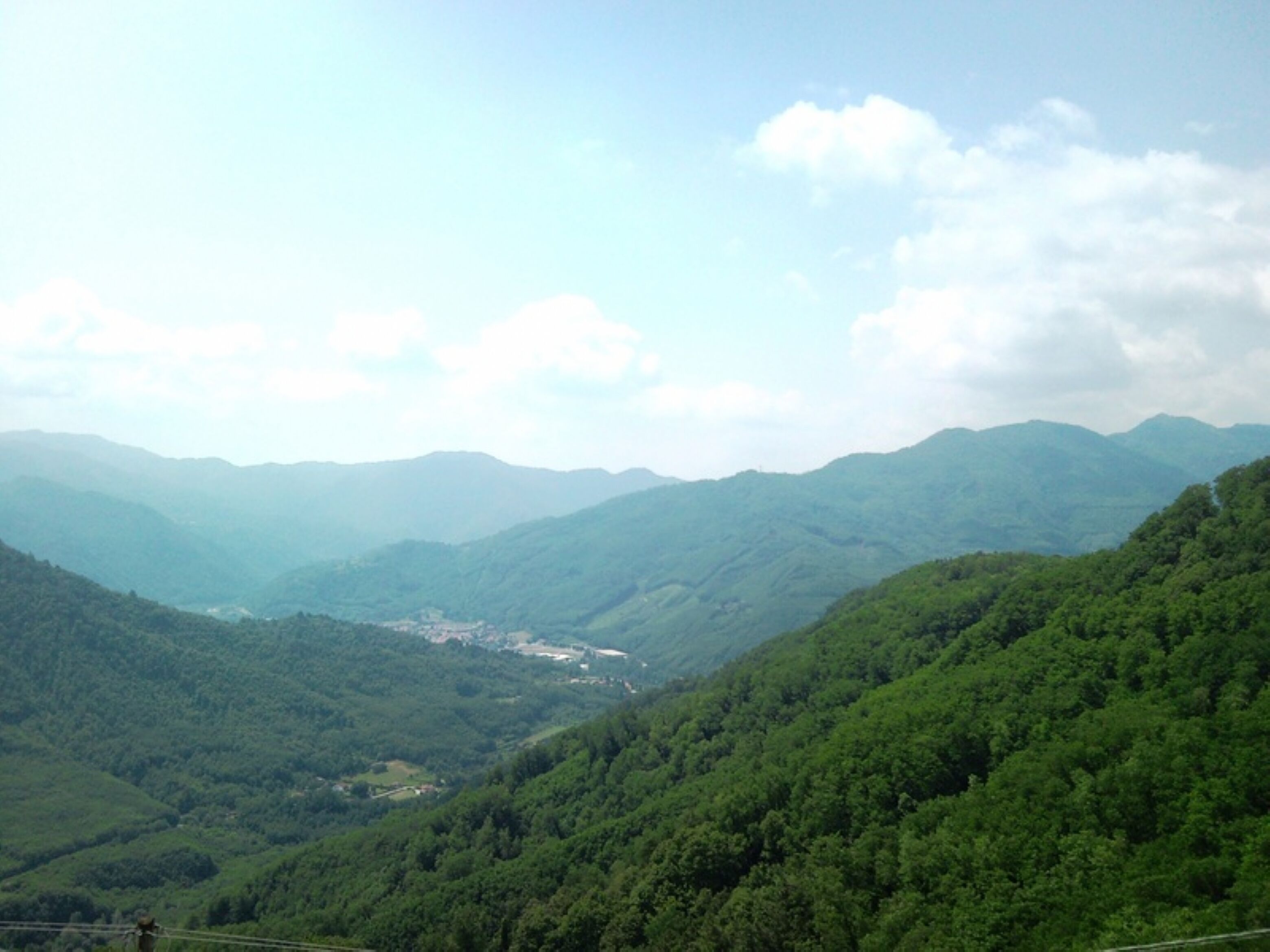 A mountainous landscape with dense green forests and a valley.