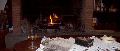 Un salón acogedor con chimenea, una mesa redonda de madera, una copa de vino y una estantería.