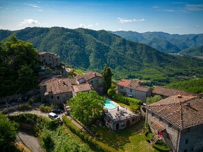 Un pueblo con edificios de piedra, una piscina y colinas verdes exuberantes al fondo.