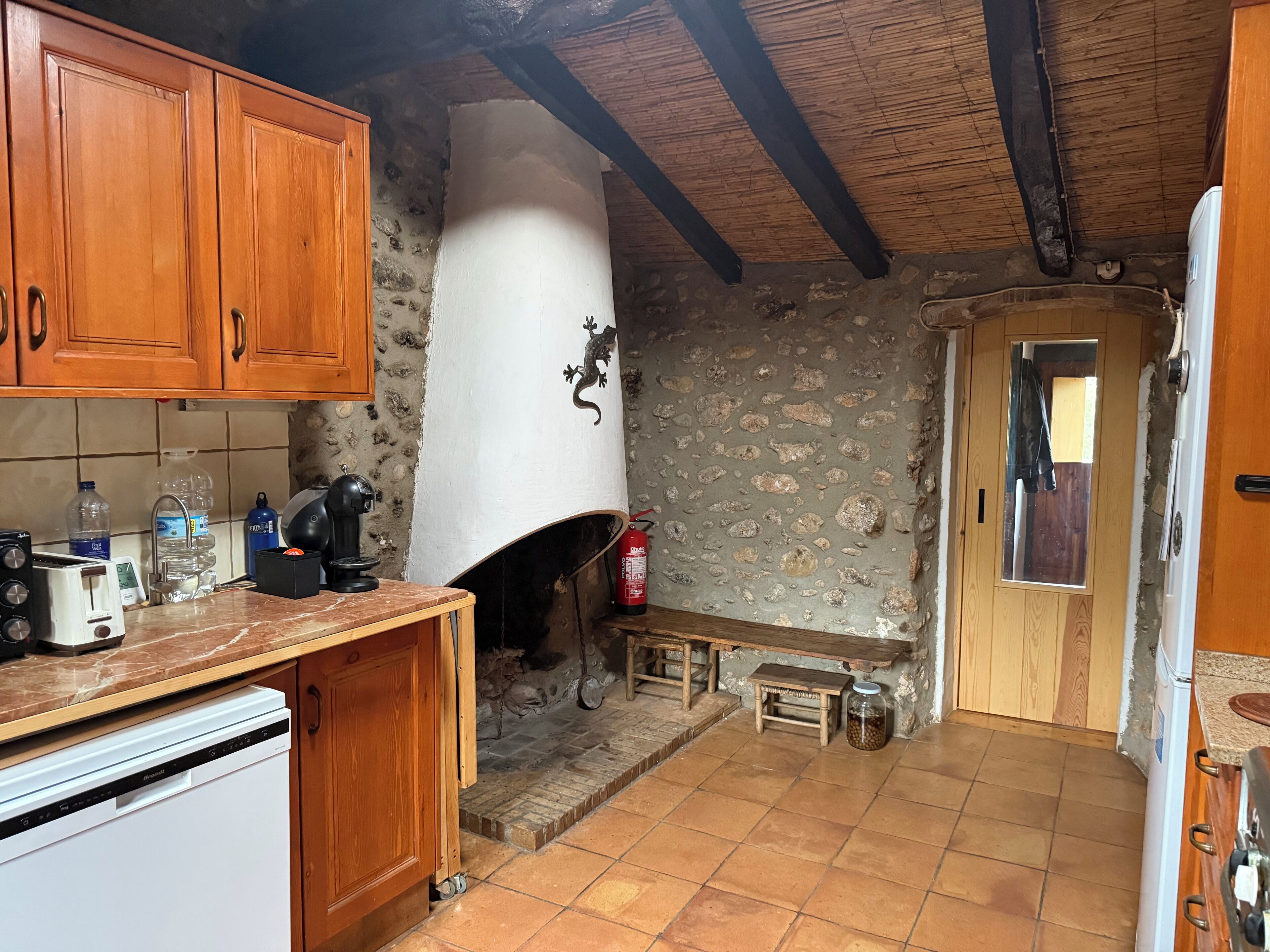 Une cuisine rustique avec des meubles en bois, un mur en pierre, une cheminée et un sol carrelé.