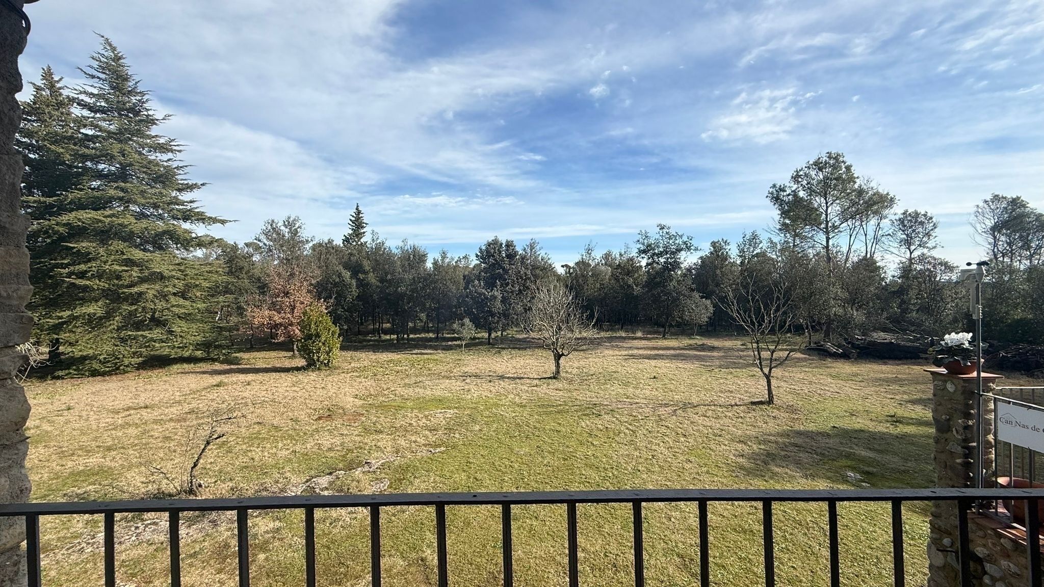 A fenced yard with a stone pillar, a view of a forest, and a clear sky.