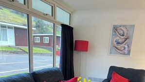 Ein modernes Wohnzimmer mit einem dunkelblauen Sofa und Sessel, roten Kissen, einer roten Stehlampe und einem Gemälde an der Wand.