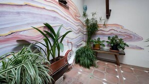 Een kamer met een grote abstracte muurschildering, een houten bank en verschillende potplanten.