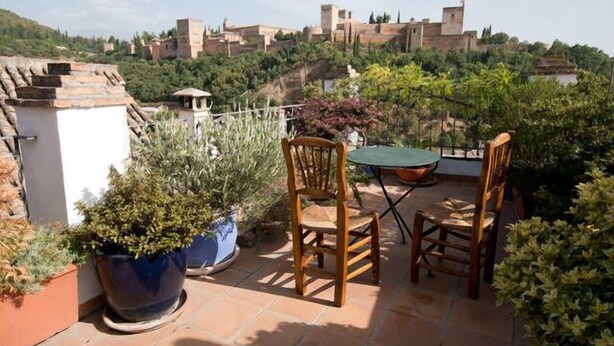 Een terras met twee houten stoelen en een tafel, omringd door planten in potten.