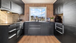 A modern kitchen with dark cabinetry, a wooden floor, and a large window offering a view of the outdoors.