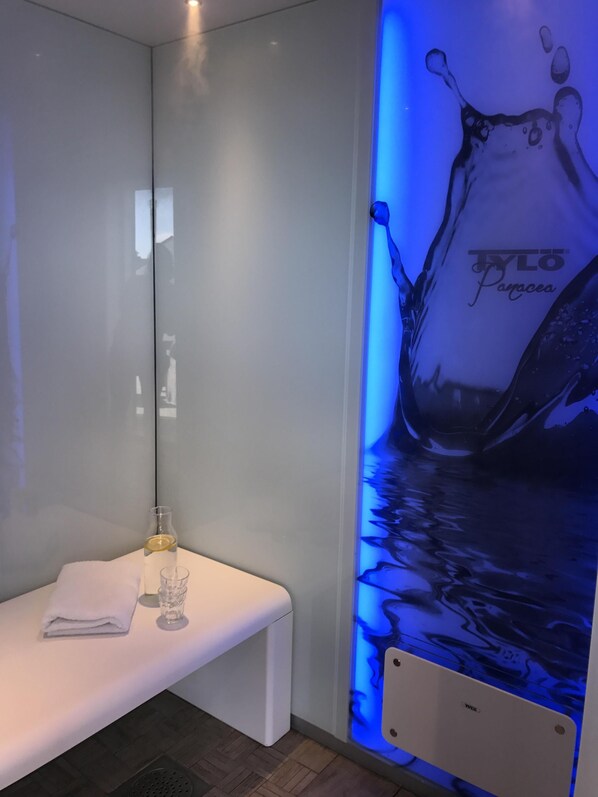 A modern bathroom with a glass partition, a bench, a towel, and a wall-mounted mirror.