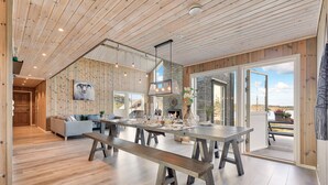 A spacious living area with a large wooden dining table, benches, and a grey sofa.