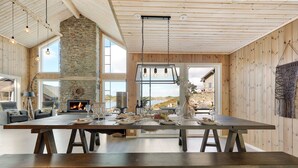 A spacious dining area with a long wooden table, stone fireplace, and large windows offering views of the beach.