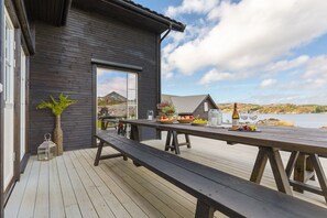Una terraza de madera con una mesa de picnic y una botella de vino, con vista a un cuerpo de agua.