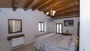 A bedroom with a wooden ceiling, a bed with patterned bedding, a bedside table, a mirror, and a poster on the wall.