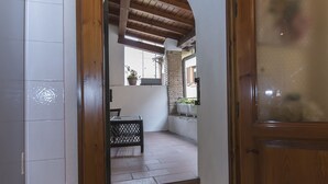 An interior hallway with a tiled floor, wooden door frames, and a view into a room with a tiled floor and a window.