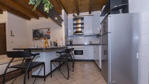 A modern kitchen with a central island, bar stools, a refrigerator, and a hanging plant.