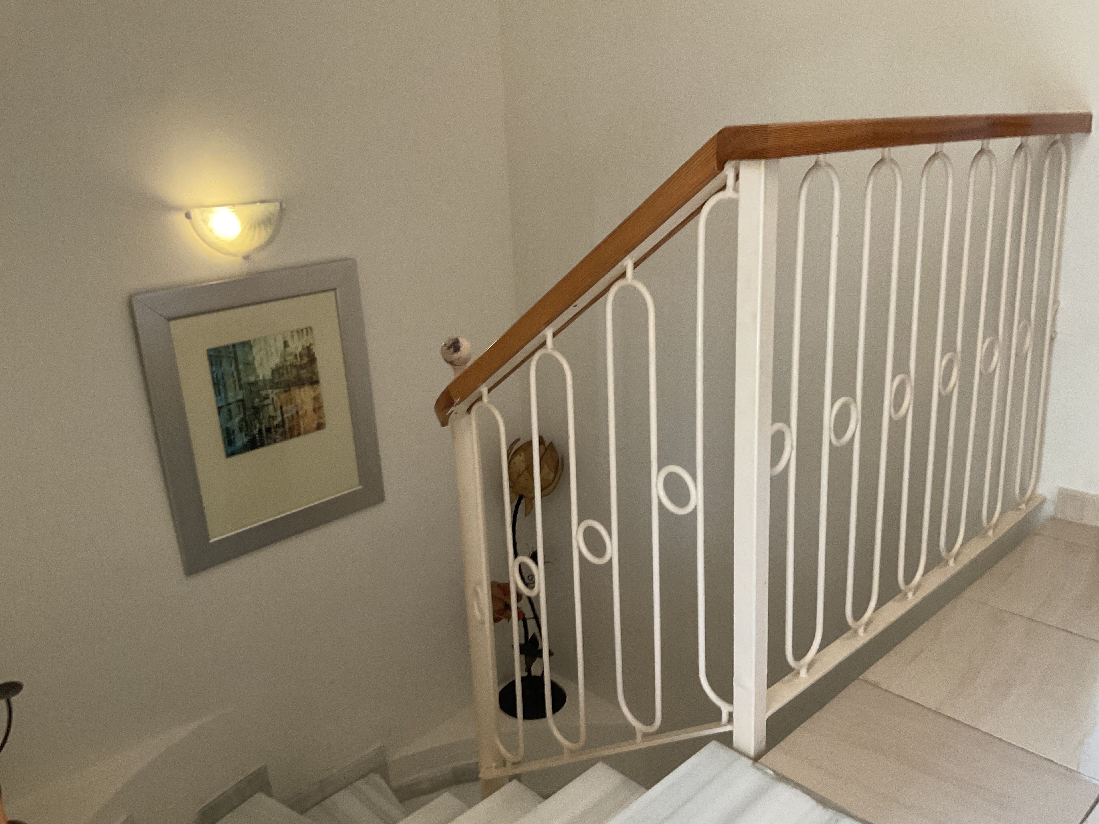 A staircase with a wooden handrail and white metal balusters, a framed picture on the wall, and a wall-mounted light fixture.