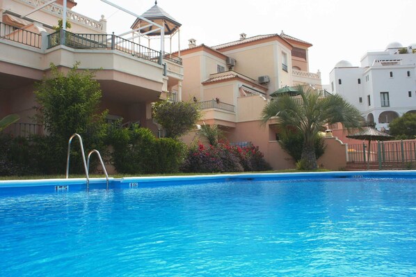 Piscina com água azul cristalina, rodeada por edifícios altos com varandas e alguma vegetação.